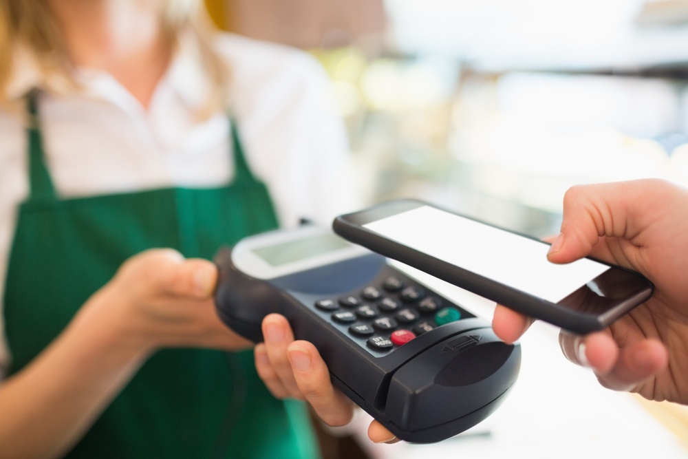 Cropped image of female worker accepting payment from customer through NFC in bakery